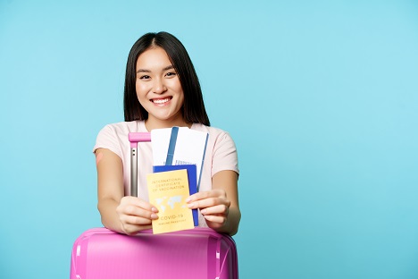 Aşı kartı, diğer seyahat dökümanları ve renkli valiziyle uçuşunu bekleyen kadın yolcu